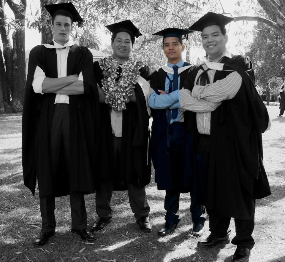 Four friends in graduation gowns and caps on the lawn at AUT