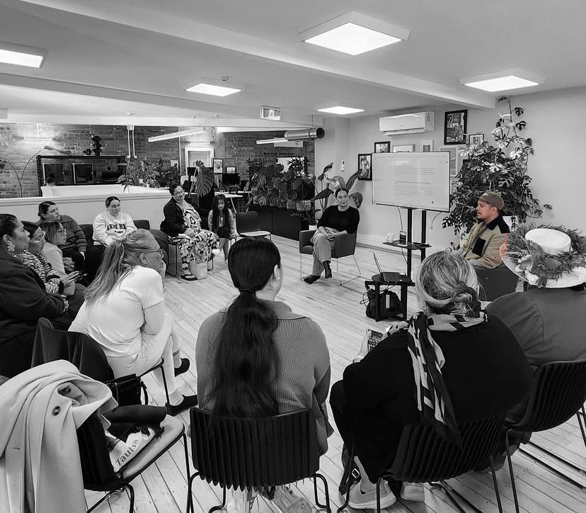 Tyrone facilitating a workshop with a seated circle of participants and a screen
